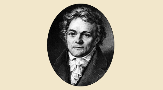 Portrait Alois Senefelder (1771-1834) Brustbild nach links im Viertelprofil. Senefelder trägt einen dunklen Gehrock mit großem Kragen, ein helles Hemd mit kleinem Kragen und einen mehrfach eng um den Hals gewundenen Stoffschal, der mit einem kunstvollen Knoten abschließt.